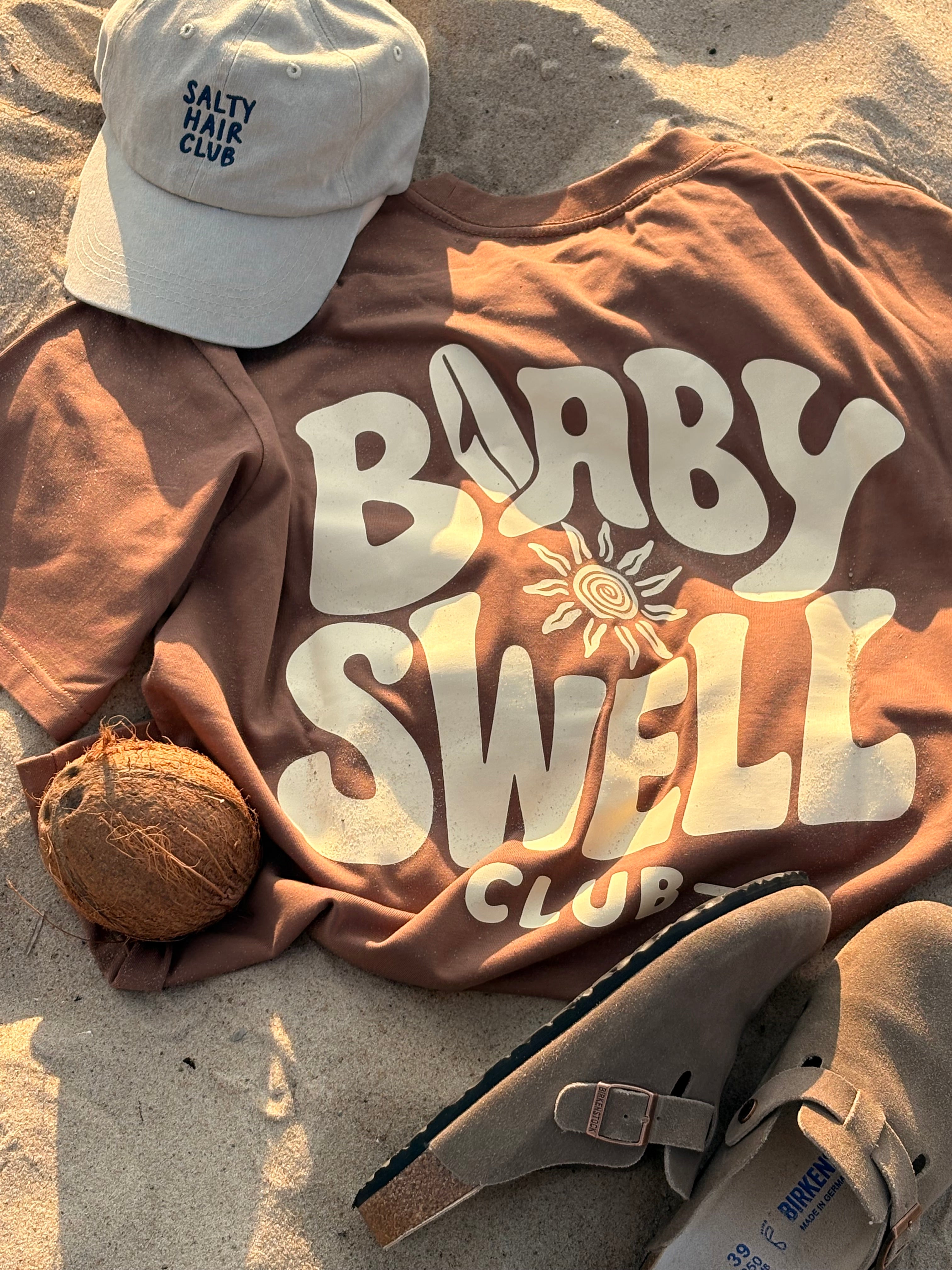 Gorra Salty Hair Club y camiseta Baby Swell Tee sobre la arena
