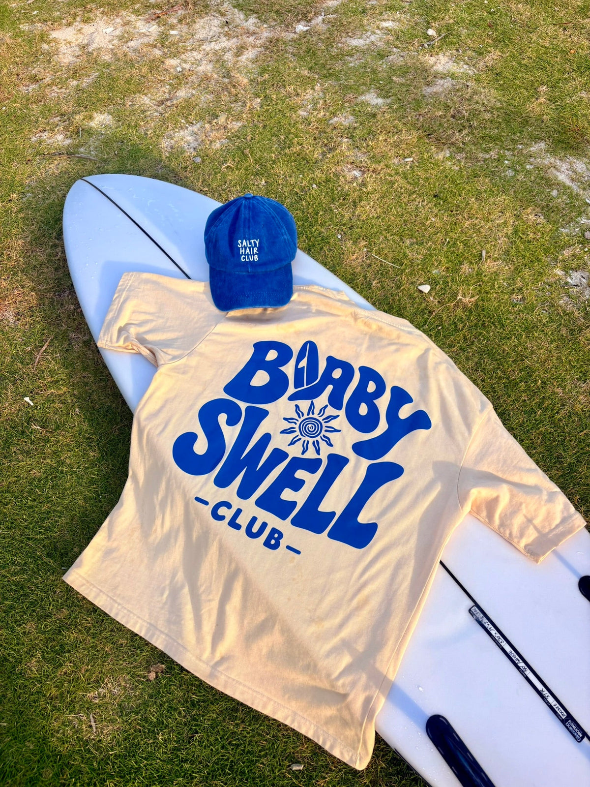 Pack Baby Swell Tee + Salty Hair Club Cap, foto lifestyle en tabla de surf